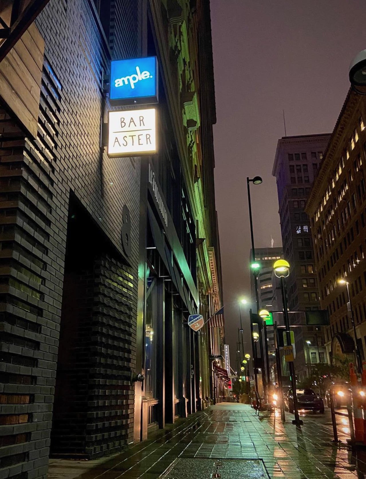 The lit Ample sign above the Bar Aster sign on a rainy downtown Cincinnati sidewalk at night