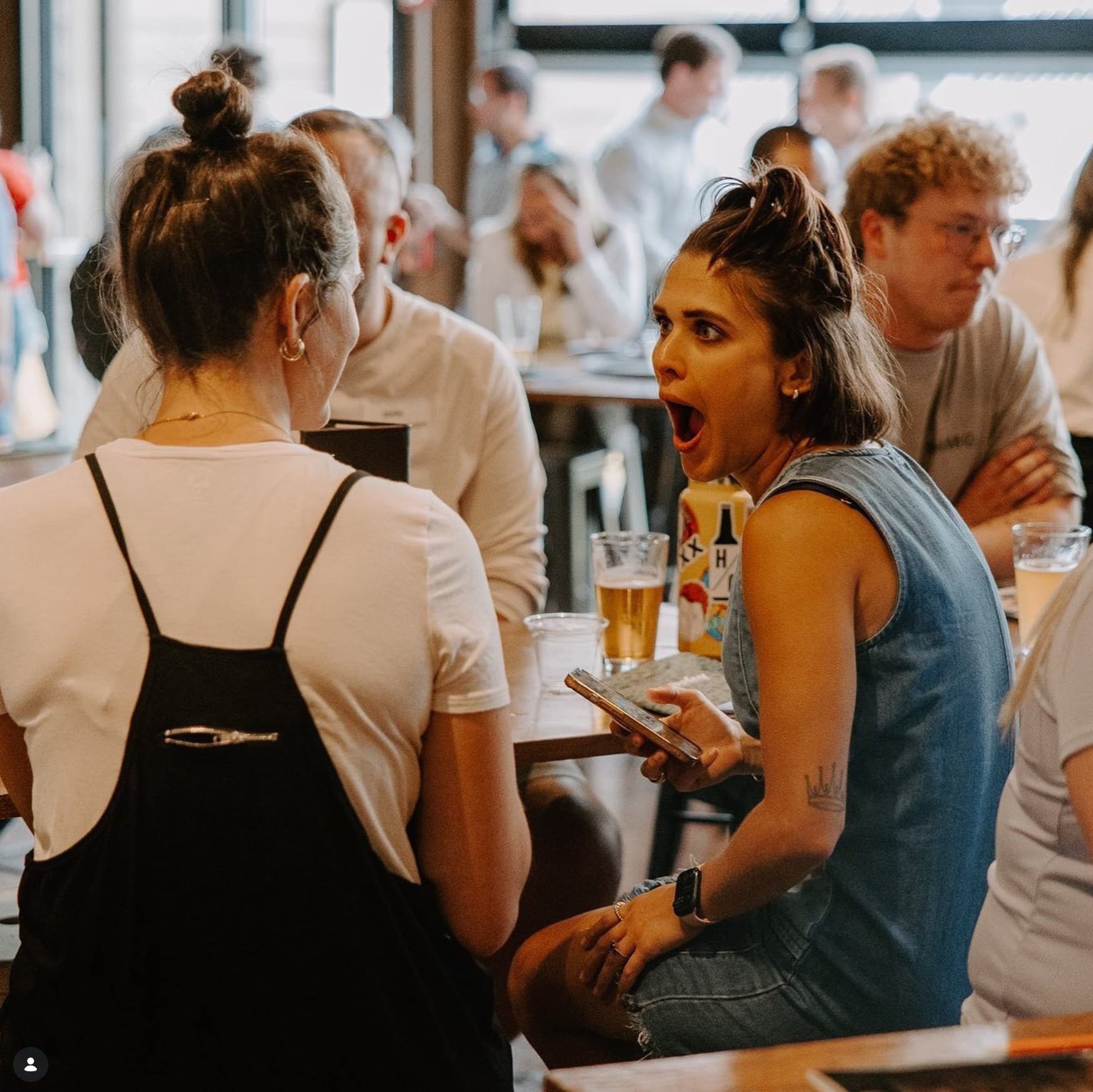 An Ample team member at a crowded bar table, mid-gasp, phone in hand