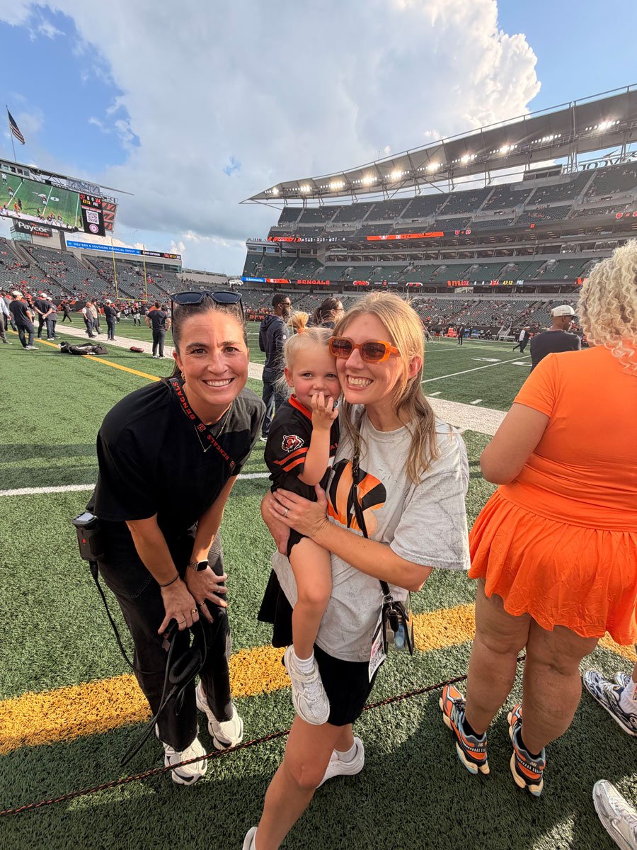 Two Ample team members and a toddler on the field before a Bengals game