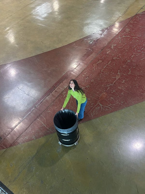 An Ample team member looking up at the camera from a wide painted floor, hauling a bin across it