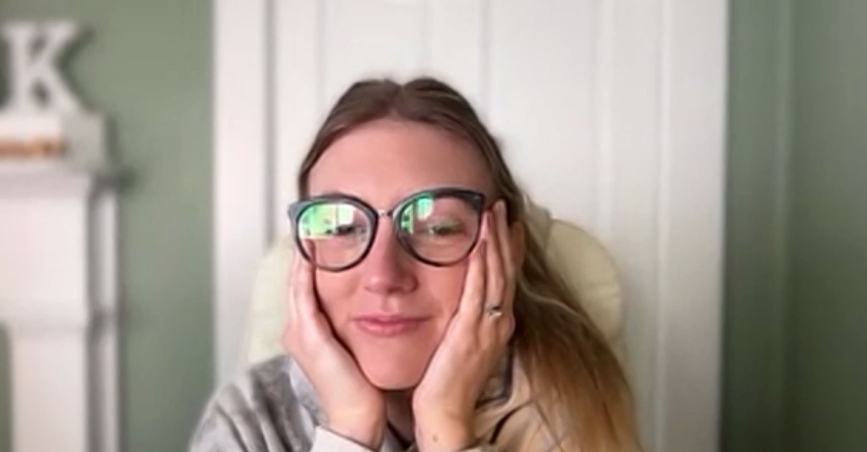 An Ample team member on a video call, chin in her hands, grinning behind her glasses