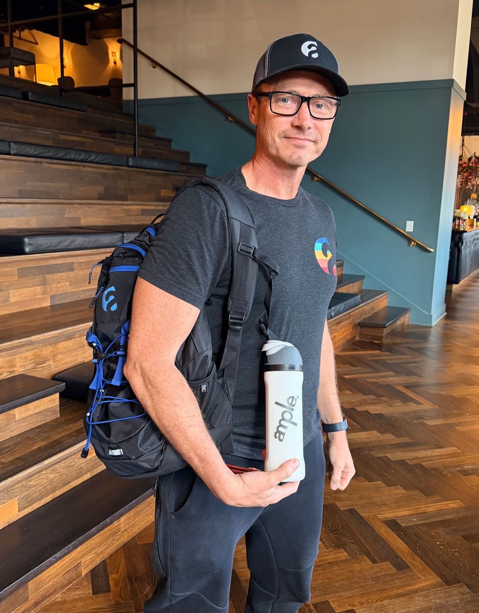 An Ample team member in an Ample cap and tee, backpack on, holding up an Ample water bottle on a staircase