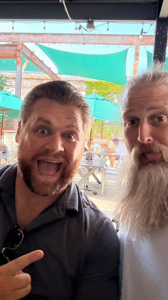 Two Ample team members mugging for a selfie on a patio, one pointing at the other’s long white beard