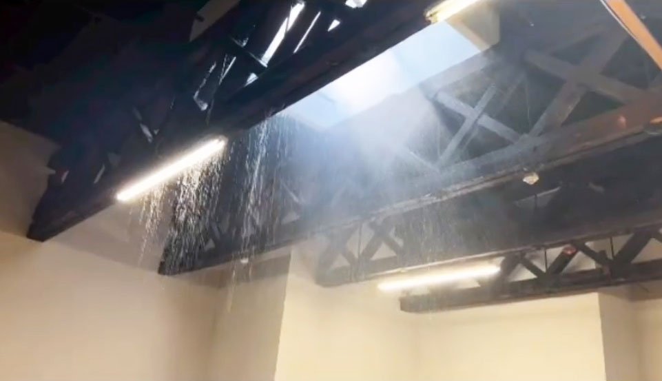 Water pouring through the exposed ceiling trusses of an empty office space